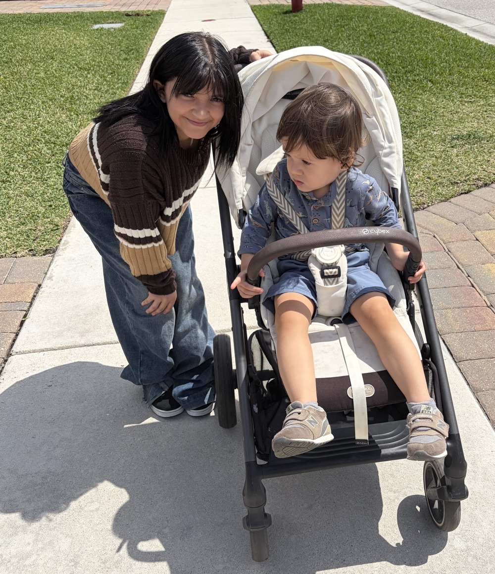 Lillyana leaning in with a smile beside a toddler in a stroller during a neighborhood walk